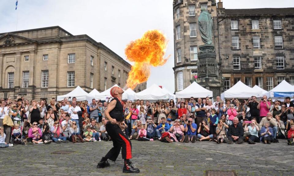 A street performer fire-eating in front of a large  crowd at the festival in pre-pandemic times.