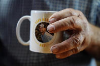 Larry Guess holds a mug with his son David Guess' face on Thursday, June 23, 2022, in Athens, Ala. Guess says he uses the mug for coffee everyday and still can't believe his son is gone. David Guess was killed by gun violence in March. (AP Photo/Brynn Anderson)