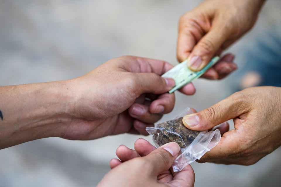 Two pairs of hands exchanging money and marijuana inside a small plastic bag.