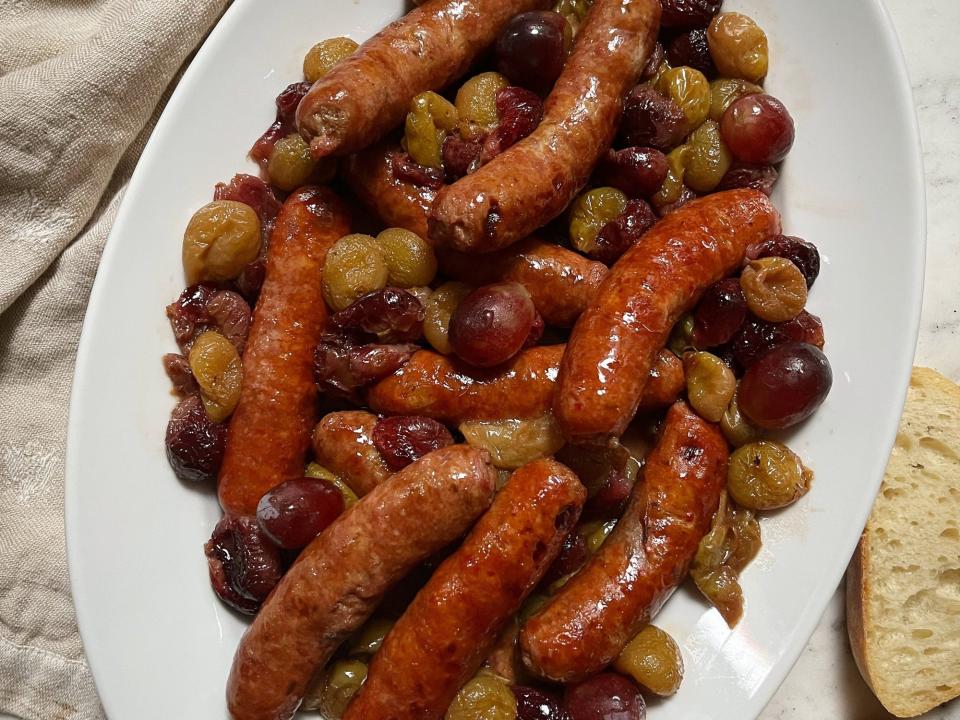 Sausages on top of roasted grapes on plate