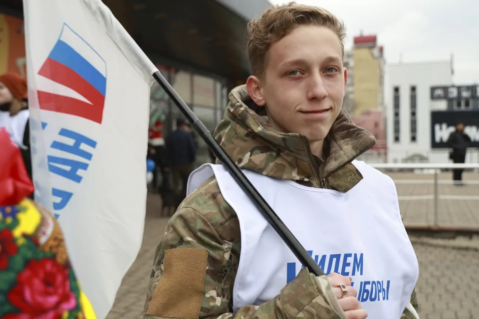 A volunteer holds a flag reading "let's go to the elections" promoting the upcoming presidential election in a street in Donetsk, the capital of Russian-controlled Donetsk region, eastern Ukraine, on Thursday, March 14, 2024. Russian President Vladimir Putin Thursday called on people in Ukraine's occupied regions to vote, telling them and Russians that participation in the elections is "manifestation of patriotic feeling," Presidential elections are scheduled in Russia for March 17. (AP Photo)