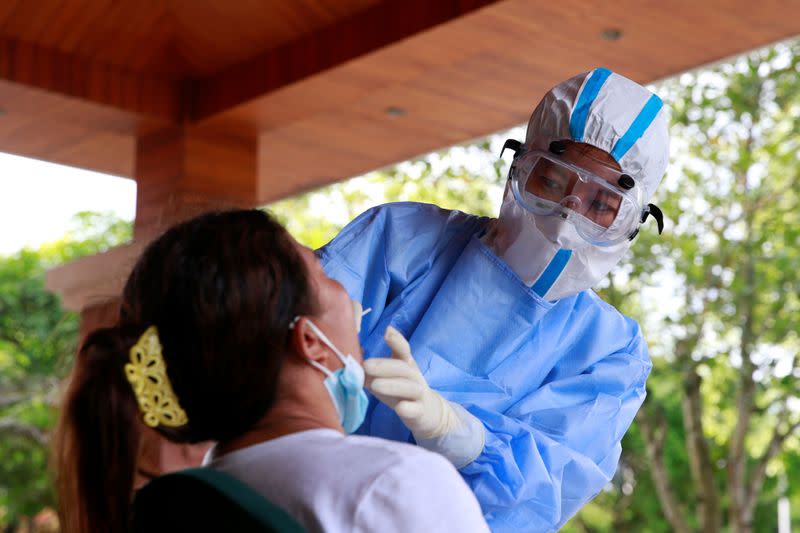 Medical worker in protective suit collects a swab sample from a woman for nucleic acid testing in the border city of Ruili