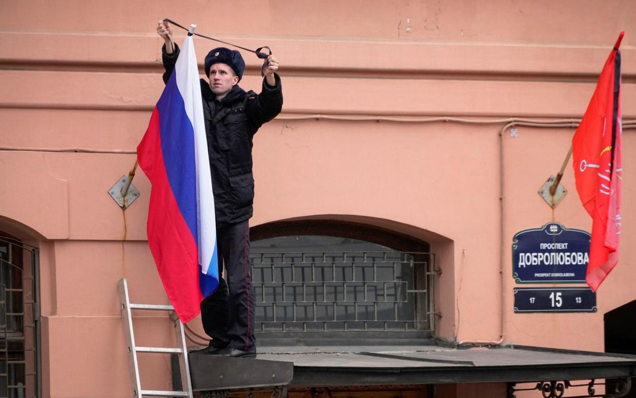 A police officer ties a mourning ribbon to a Russian flag in St. Petersburg, Russia.