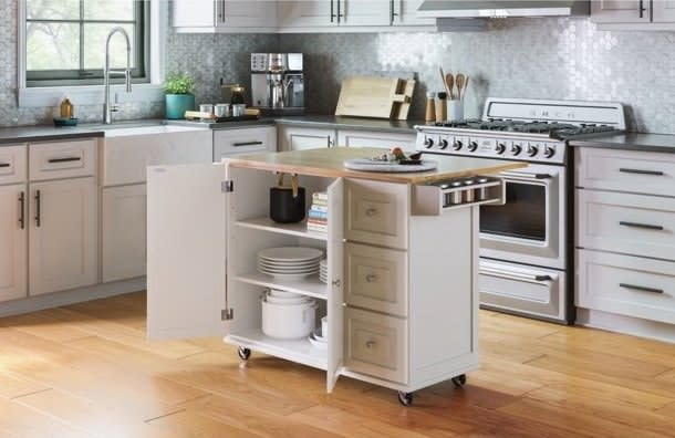 A modern kitchen with a rolling island cart stocked with kitchenware and positioned near the cooking range