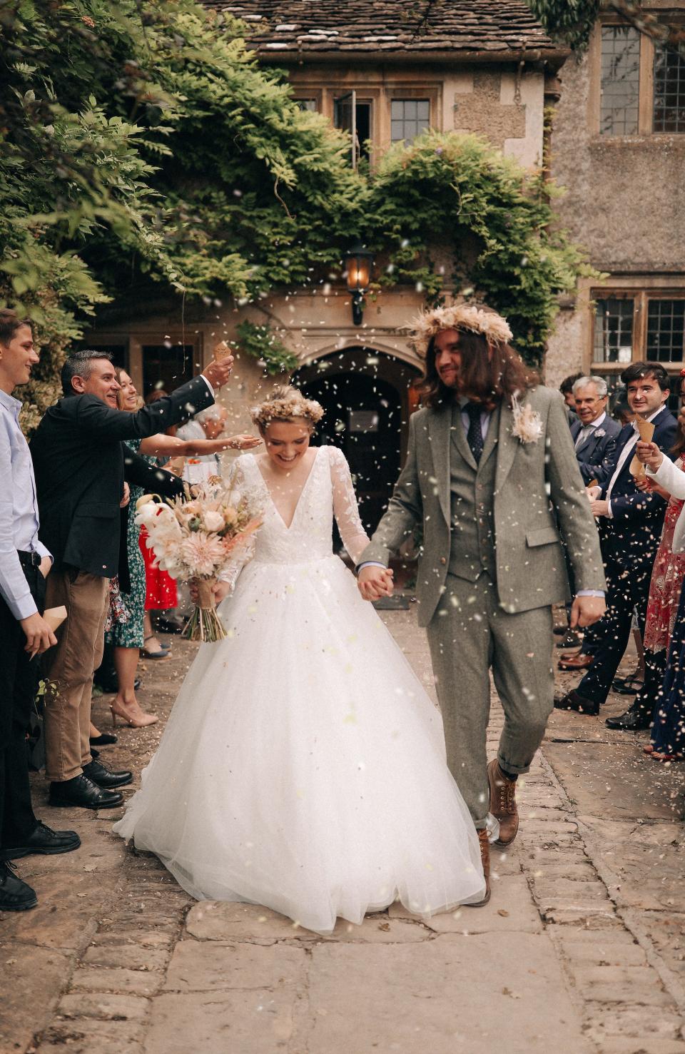 A couple holds hands and leaves their wedding ceremony as people throw flower petals over them.