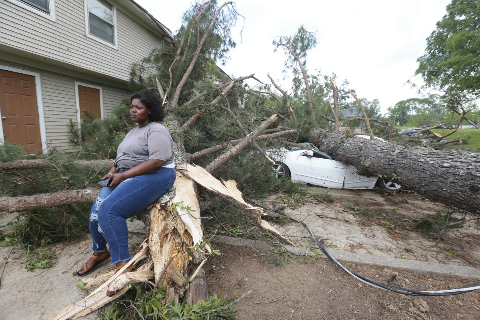 Myesha Gore of Calhoun City, Miss., sits on the trunk of a shattered pine tree Monday, May 3, 2021, as the rest of the tree crushed her car behind her while she was visiting her mother in Vardaman during Sunday's severe weather. (Thomas Wells/The Northeast Mississippi Daily Journal via AP)