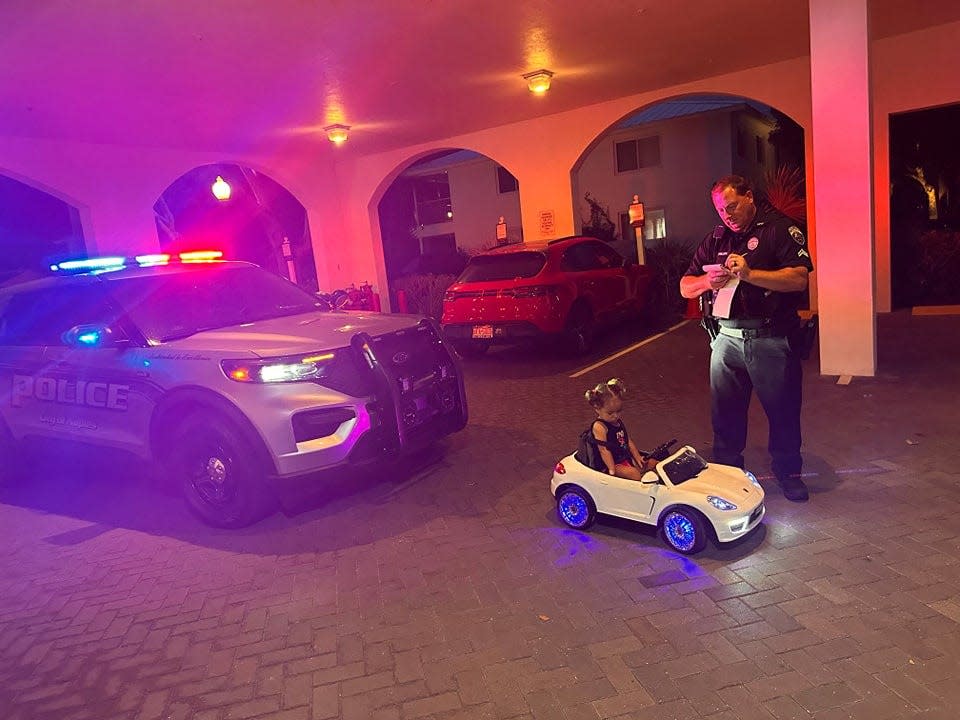Photo of a Naples police officer pretending to write a ticket to a child driving a toy car.