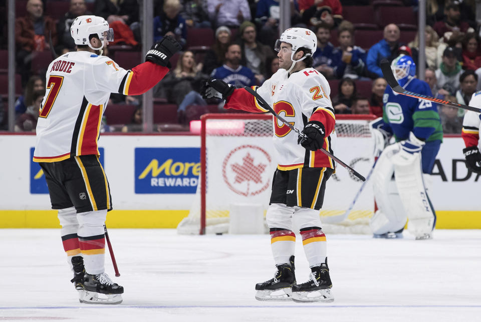 Calgary Flames' T.J. Brodie, left, and Dillon Dube celebrate Dube's goal against Vancouver Canucks goalie Jacob Markstrom, back right, of Sweden, during the second period of an NHL hockey game Saturday, Feb. 8, 2020, in Vancouver, British Columbia. (Darryl Dyck/The Canadian Press via AP)
