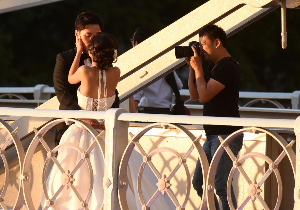 A photographer takes pictures of a newlywed couple kissing on Cavenagh bridge along the Singapore river on 16 April 2015. PHOTO: Roslan Rahman/AFP