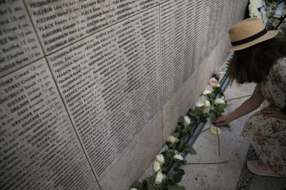 A woman lays a flower on the Wall of Names during a ceremony at the memorial garden of the children of the Vel d'Hiv Roundup in Paris, July 16, 2022. (AP Photo/Christophe Ena)