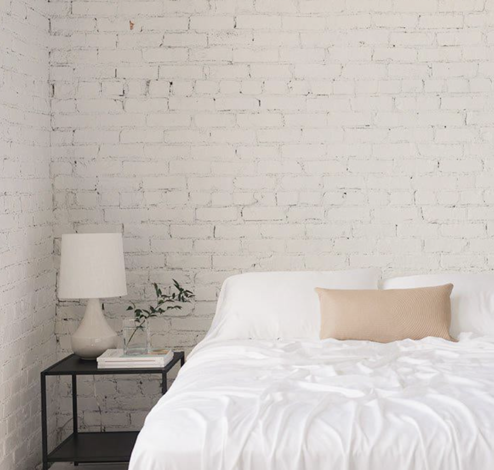 Bamboo Sheet Set in white on bed against white brick wall and lamp (Photo via Cozy Earth)