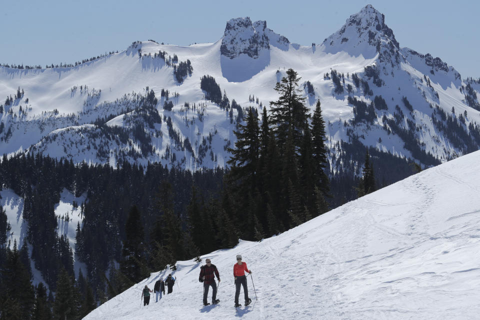 FILE - In this March 18, 2020, file photo, snowshoers head up a slope above Paradise at Mount Rainier National Park in Washington state. As the coronavirus pandemic continues, the National Park Service is testing public access at several parks across the nation with limited offerings and services. (AP Photo/Ted S. Warren, File)