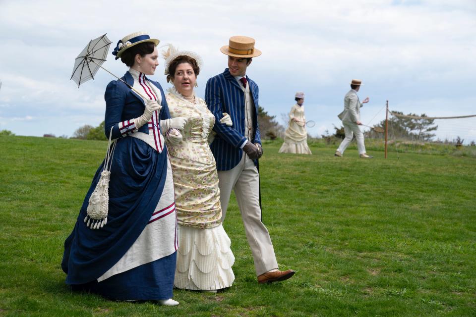 Actors Amy Forsyth (as Caroline “Carrie” Astor), left, Ashlie Atkinson (Mamie Fish) and Harry Richardson (Larry Russell) stroll across the lawn of The Ledges in Newport in the HBO drama "The Gilded Age." The series premieres Monday  at 9 p.m.