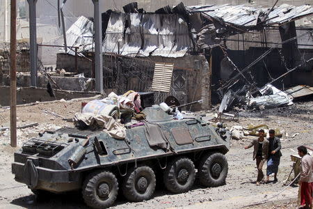 Men walk past a police vehicle along a street damaged by an air strike on Monday that hit a nearby army weapons depot, in Sanaa April 21, 2015. REUTERS/Mohamed al-Sayaghi