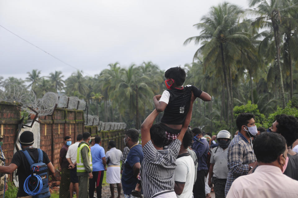 People gather to look at the Air India Express flight that skidded off a runway while landing at the airport in Kozhikode, Kerala state, India, Saturday, Aug. 8, 2020. The special evacuation flight bringing people home to India who had been trapped abroad because of the coronavirus skidded off the runway and split in two while landing in heavy rain killing more than a dozen people and injuring dozens more. (AP Photo/C.K.Thanseer)