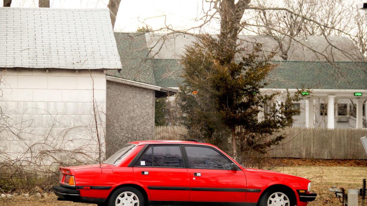 a red peugeot 505 v6 stx parked in front of a house