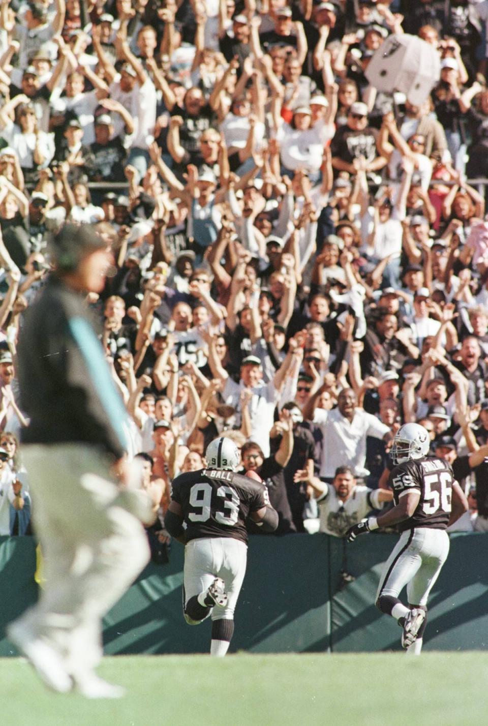 Oakland fans stand and cheer as Raiders defensive tackle Jerry Ball (93) runs into the end zone for a touchdown, after making an interception late in the fourth quarter of an NFL football game on September 15, 1996. Jaguars Head Coach Tom Coughlin, at left, stands frustrated on the field. [Rick Wilson/Florida Times-Union]