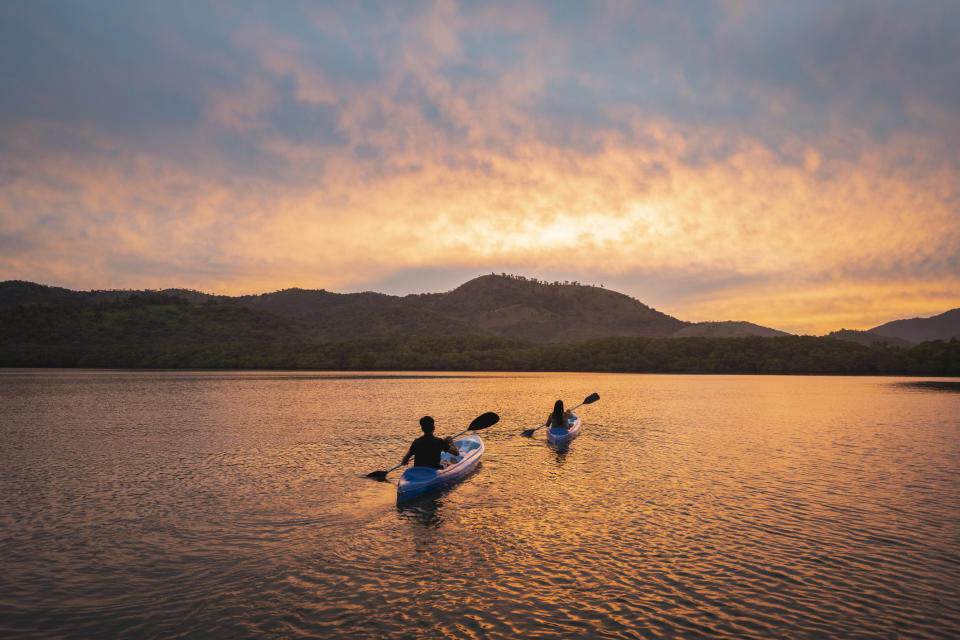 Two kayakers paddling in a large body of water at sunset
