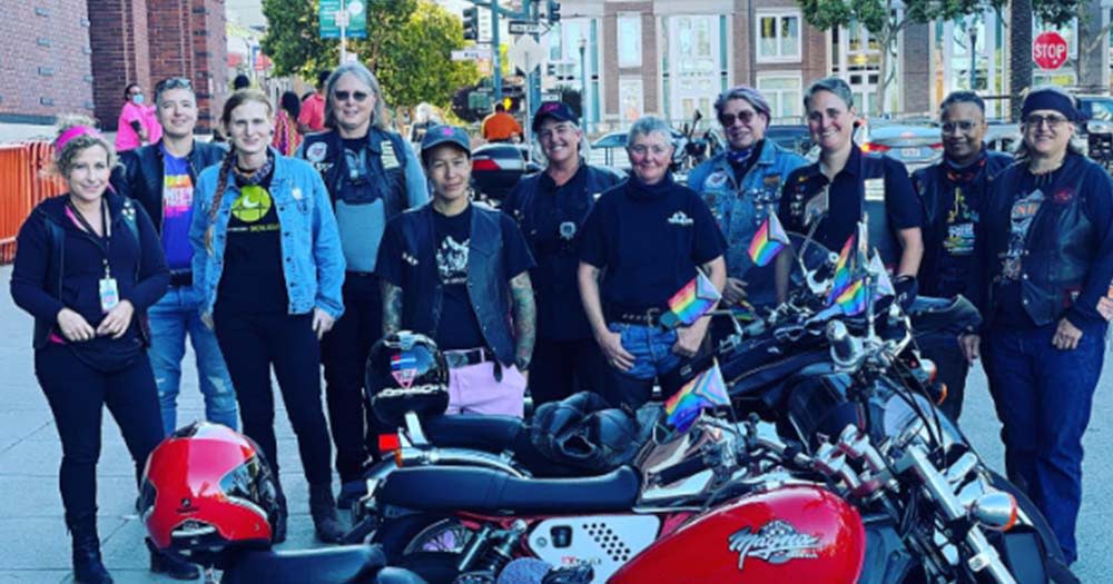 Several Dykes with Bikes butch women dressed in black pose with motor bike.