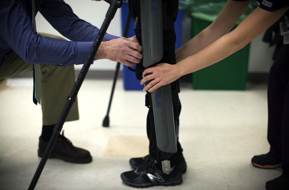Allan Kozlowski (L) , assistant professor of Rehabilitation Medicine at Icahn School of Medicine at Mount Sinai hospital, and Alexandra Voigt (R), a clinical research coordinator and therapist, adjust a ReWalk electric powered exoskeletal suit before a therapy session to 22-old Errol Samuels from Queens, New York, who lost the use of his legs in 2012 after a roof collapsed onto him, at Mount Sinai Hospital in New York March 26, 2014. ReWalk, made by the Israeli company Argo Medical Technologies, is a computer controlled device that powers the hips and knees to help those with lower limb disabilities and paralysis to walk upright using crutches. Kozlowski, whose patients are working with the ReWalk and another exoskeleton, the Ekso (Ekso Bionics) hopes machines like these will soon offer victims of paralysis new hope for a dramatically improved quality of life and mobility. The ReWalk is currently only approved by the U.S. Food and Drug Administration (FDA) for use in rehabilitation facilities like at Mount Sinai, as they weigh whether to approve the device for home use as it already is in Europe. Picture taken March 26, 2014. REUTERS/Mike Segar