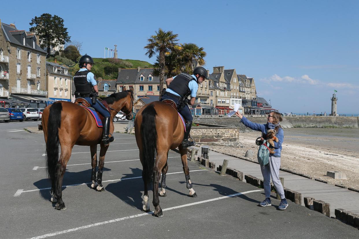 Police officers on horses check documents as they patrol the street during a nationwide confinement to counter COVID-19 in the coastal town of Cancale, western France on Saturday, April 11, 2020.