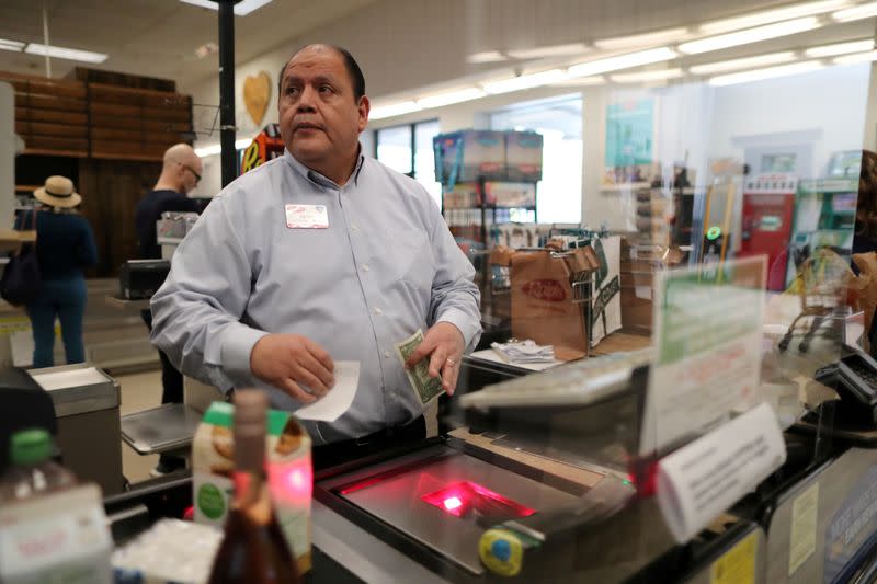 Assistant store manager Jesus Alvarez rings up groceries from behind a new plexiglass barrier at Ralphs Kroger grocery store after California issued a stay-at-home order in an effort to prevent the spread of coronavirus disease (COVID-19), in Los Angeles