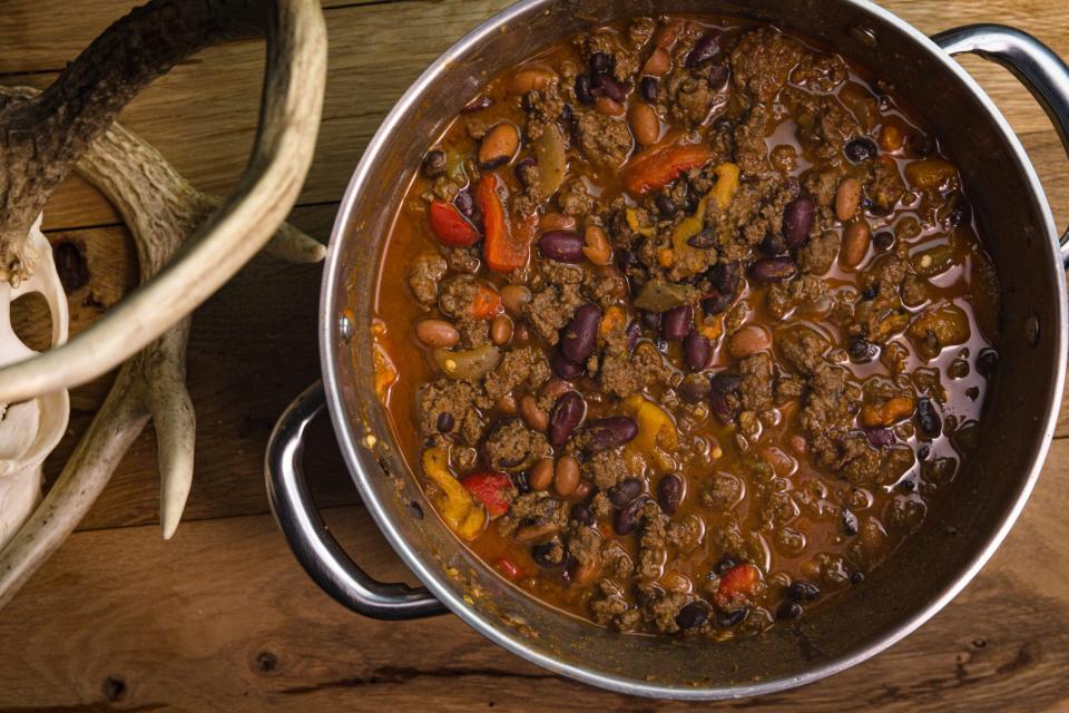 A bowl of venison chili resting on a wooden table next to a deer skull.