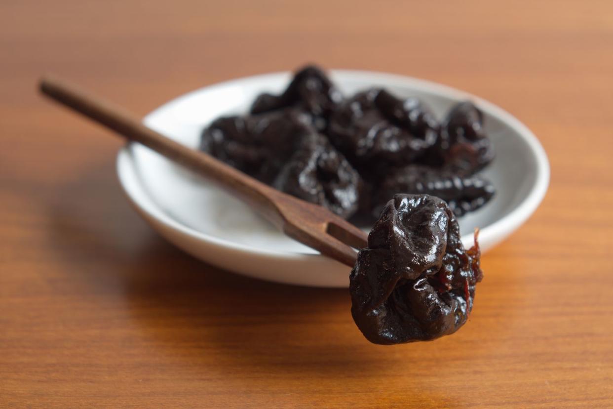 prunes in a white bowl with a wooden fork on a wooden table