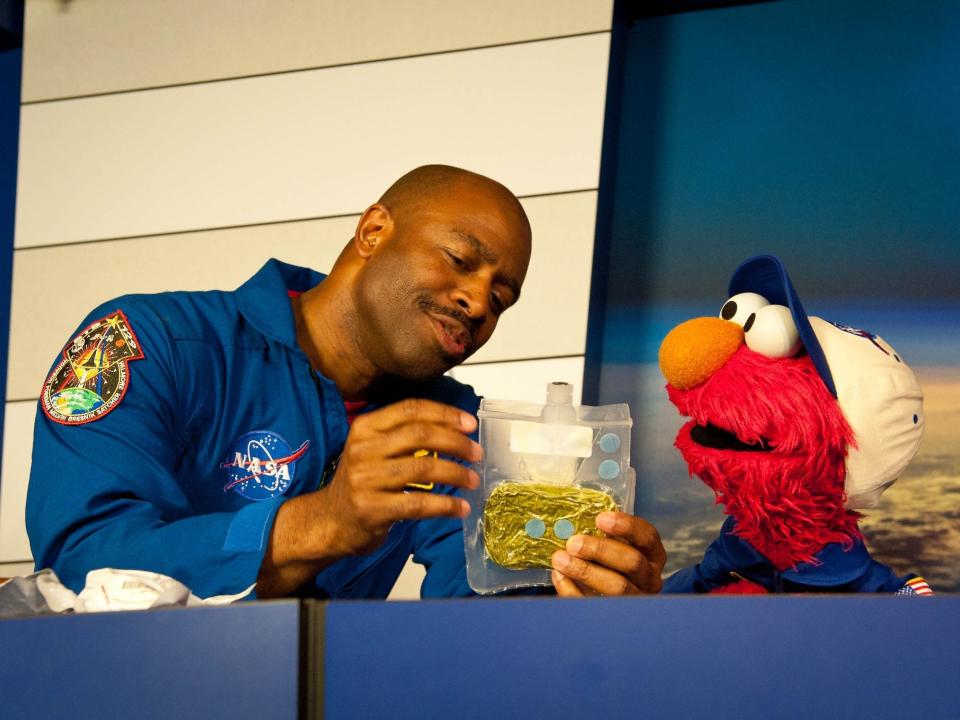 Der ehemalige Astronaut Leland Melvin zeigt Elmo aus der Sesamstraße im Kennedy Space Center der NASA dehydrierte Lebensmittel. - Copyright: NASA/Carla Cioffi