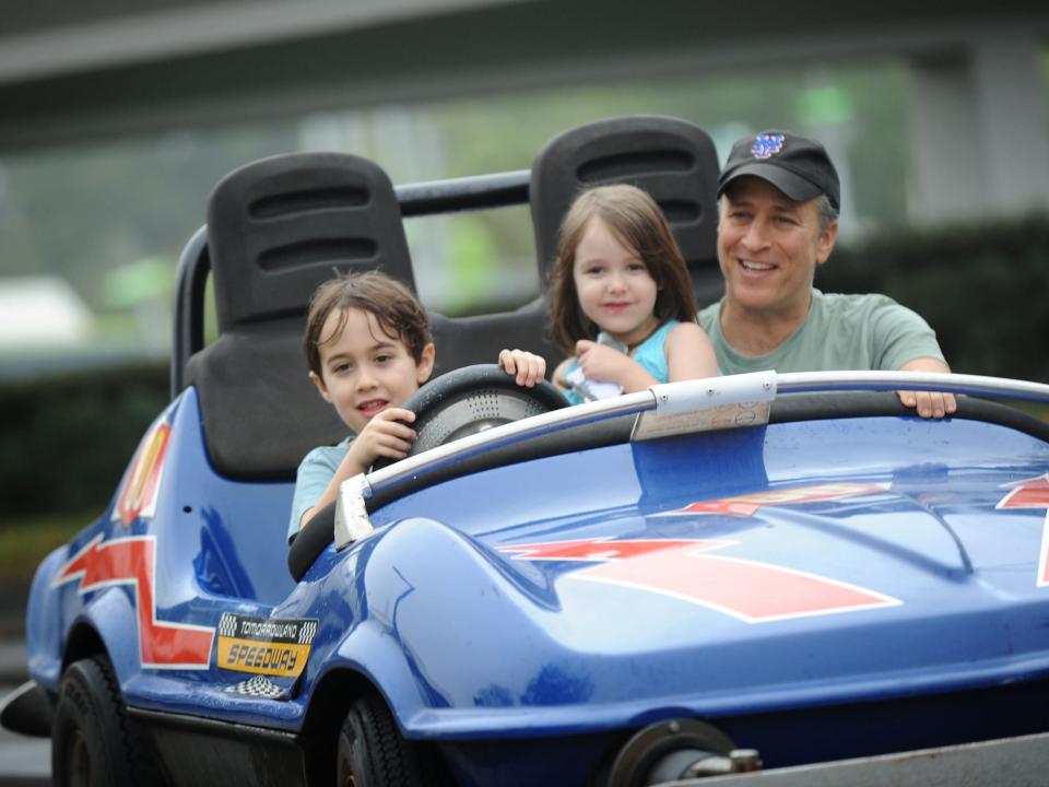 Comedian Jon Stewart takes a ride on the Tomorrowland Indy Speedway with his children Natel left, age 6, and Maggie, center, age 5, in 2011.