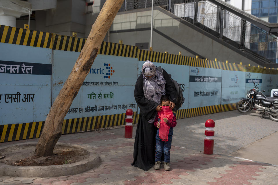 A woman covers the face of her child with a scarf at a bus terminal in New Delhi, India, Wednesday, March 24, 2021. (AP Photo/Altaf Qadri)