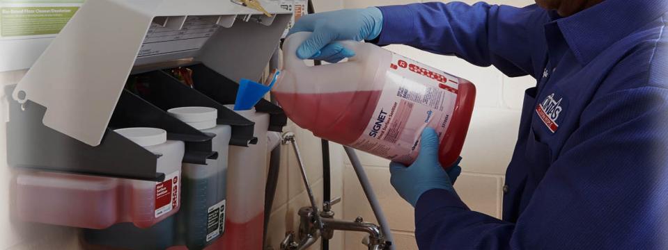 Person in Cintas uniform pouring red liquid into a dispenser.