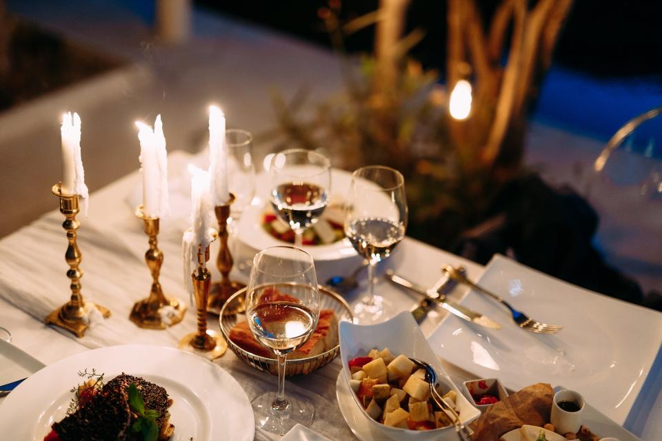 Table with burning candles in candlesticks, glasses and food outside in the evening.