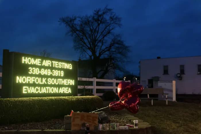 at night, red heart balloons sit next to a lit up sign that reads "home air testing 330 849 3919 norfolk souther evacuation area"