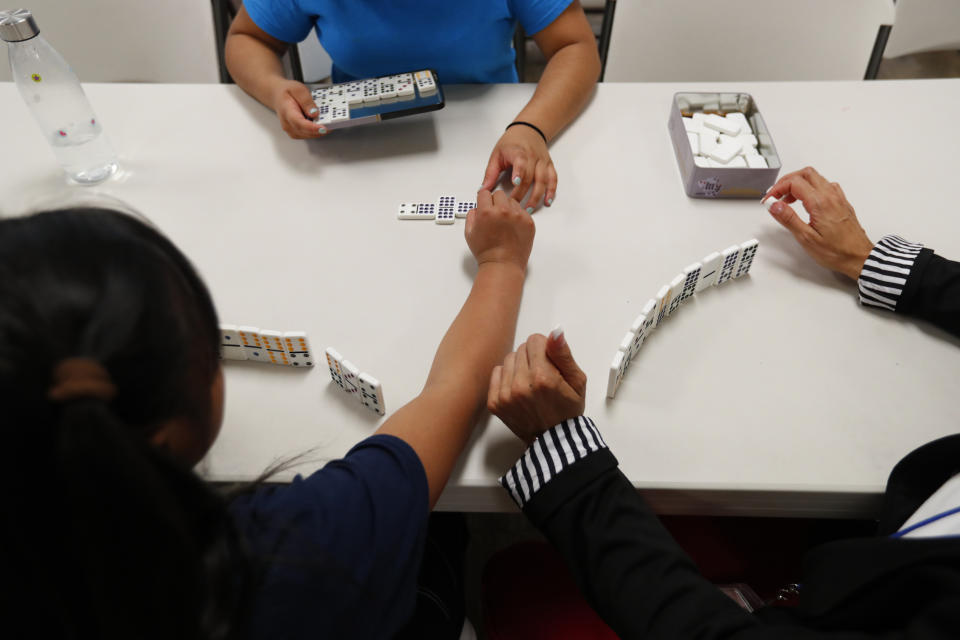 In this Sept. 24, 2019, photo, girls play dominos with a staff member at a shelter for migrant teenage girls, in Lake Worth, Fla. The nonprofit U.S. Committee for Refugees and Immigrants opened the federally funded Rinconcito del Sol shelter this summer, aiming to make it a model of excellence in a system of 170 detention centers, residential shelters and foster programs which held nearly 70,000 migrant kids in the past year. (AP Photo/Wilfredo Lee)