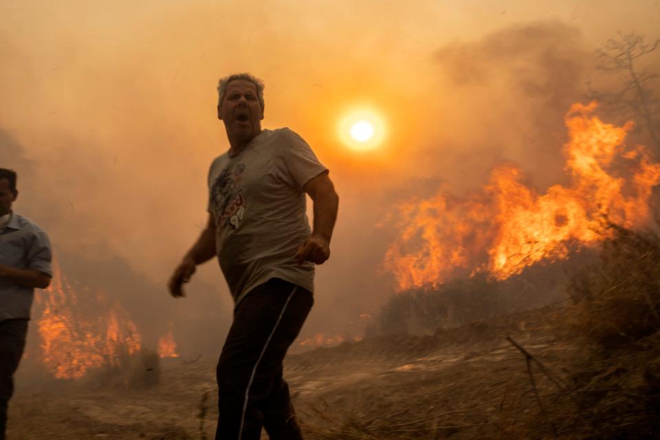 A local reacts as the flames burn trees in Gennadi village, on the Aegean Sea island of Rhodes, southeastern Greece, on Tuesday, July 25, 2023. (AP Photo/Petros Giannakouris)