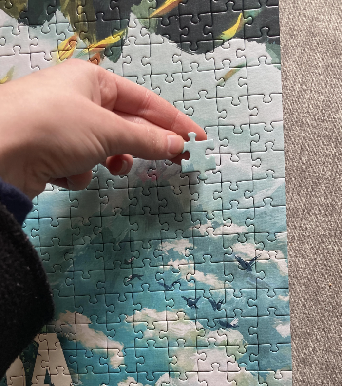 Hand placing a puzzle piece into a nearly complete jigsaw puzzle with a nature scene