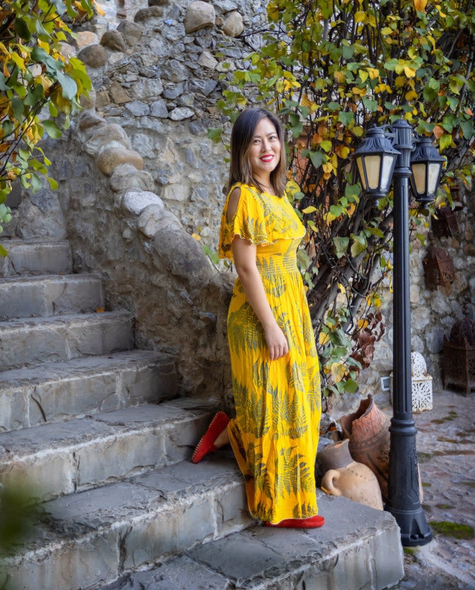 Maria Jiang, a woman with brown hair in a yellow dress with red shoes desending a flight of stairs