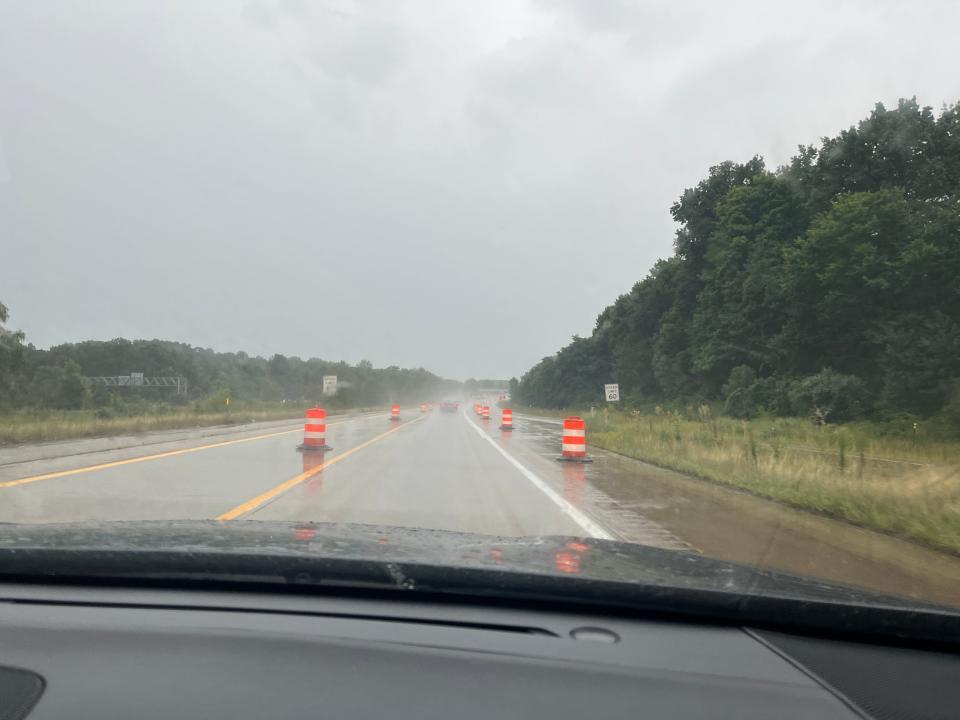 A rainy highway with traffic barrels.