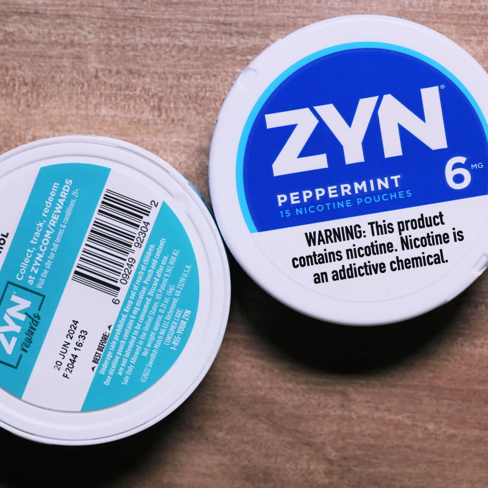 Two ZYN nicotine pouches lie on a wooden surface, on one lid is written 