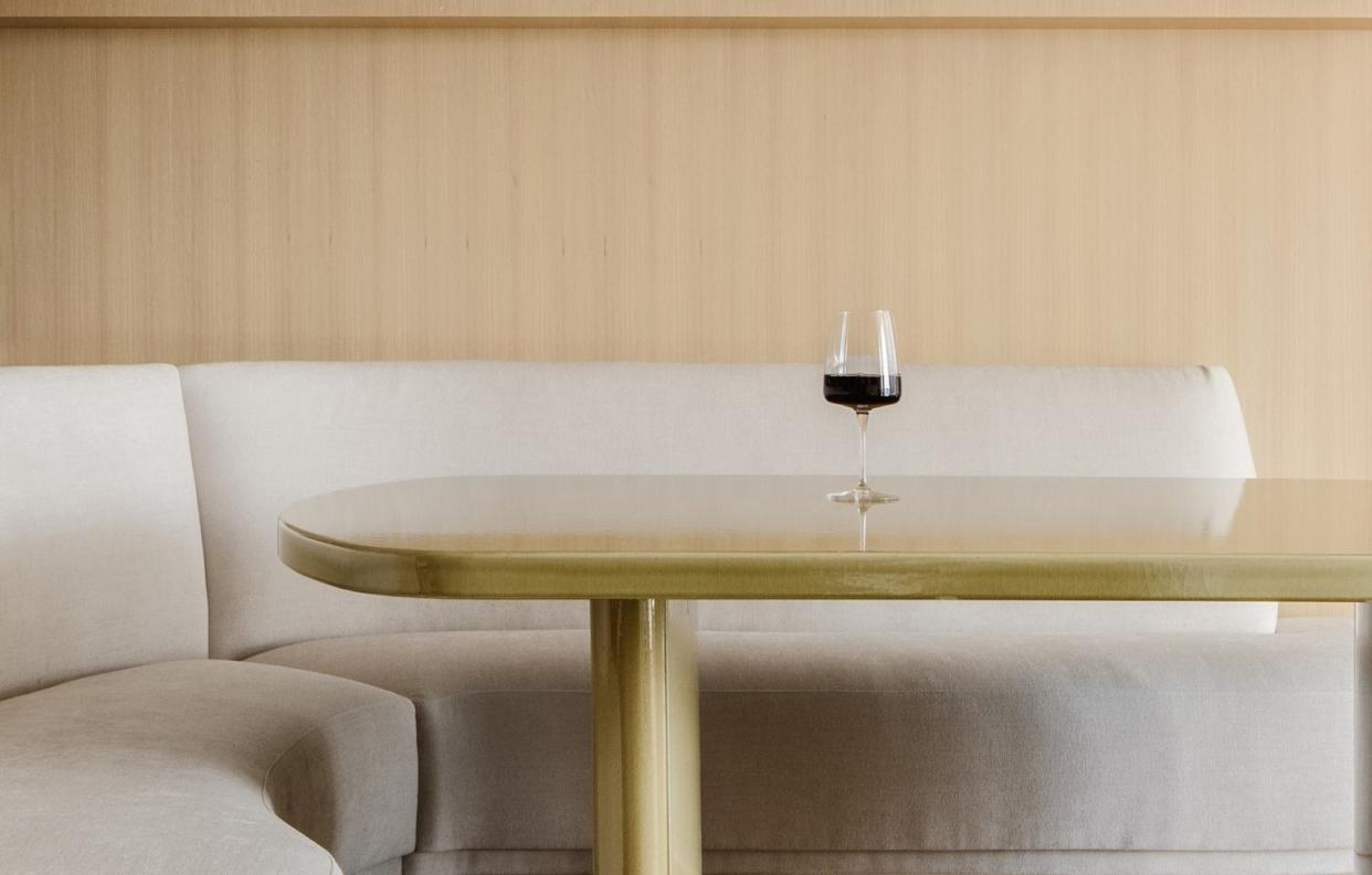  A dining table with a single wine glass kept atop. And a curving sofa surrounding it. 