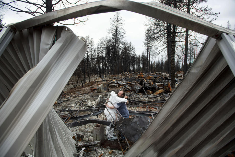 In this Feb. 8, 2019, photo, Bud Daneau hugs Carol Beall while helping her comb through her residence, destroyed by the Camp Fire, at the Ridgewood Mobile Home Park in Paradise, Calif. In the 100 days since a wildfire nearly burned the town of Paradise off the map, the long recovery is just starting. Work crews have been cutting down trees and clearing burned-out lots, but Paradise is mostly a ghost town where survivors still dig for keepsakes in the foundations of their homes. (AP Photo/Noah Berger)