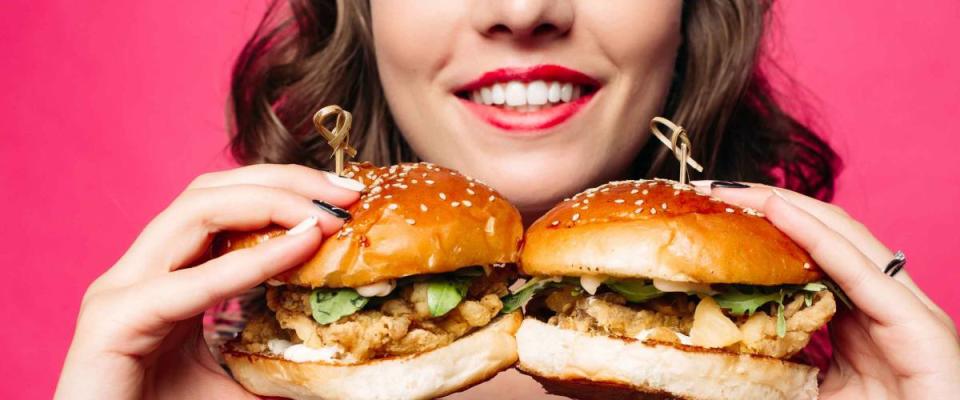 Close-up of unrecognizable brunette smiling woman holding two delicious fresh burgers with juicy roasted chicken and rocket salad.