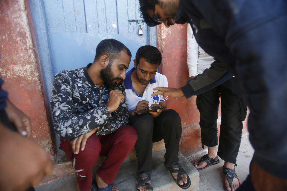 Support staff play games on a cell phone inside the premises of a school deserted school compound in Srinagar, Indian controlled Kashmir, Monday, Aug. 19, 2019. Restrictions continue in much of Indian-administered Kashmir, despite India's government saying it was gradually restoring phone lines and easing a security lockdown that's been in place for nearly two weeks. (AP Photo/Mukhtar Khan)