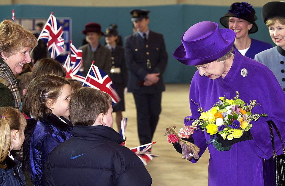 The queen in bright purple is given a beanie by two small children