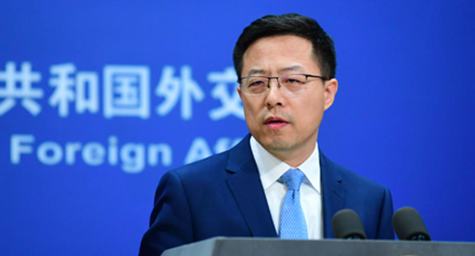 Zhao Lijian wearing a navy suit and blue tie with glasses at a Foreign Ministry press conference.