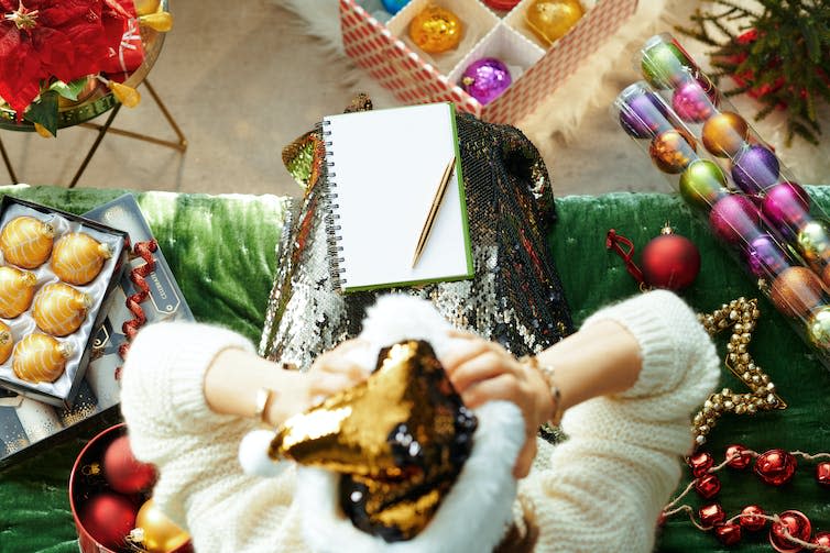 Upper view of stressed stylish housewife in sparkle gold sequin santa hat sitting on sofa in the modern living room at Christmas