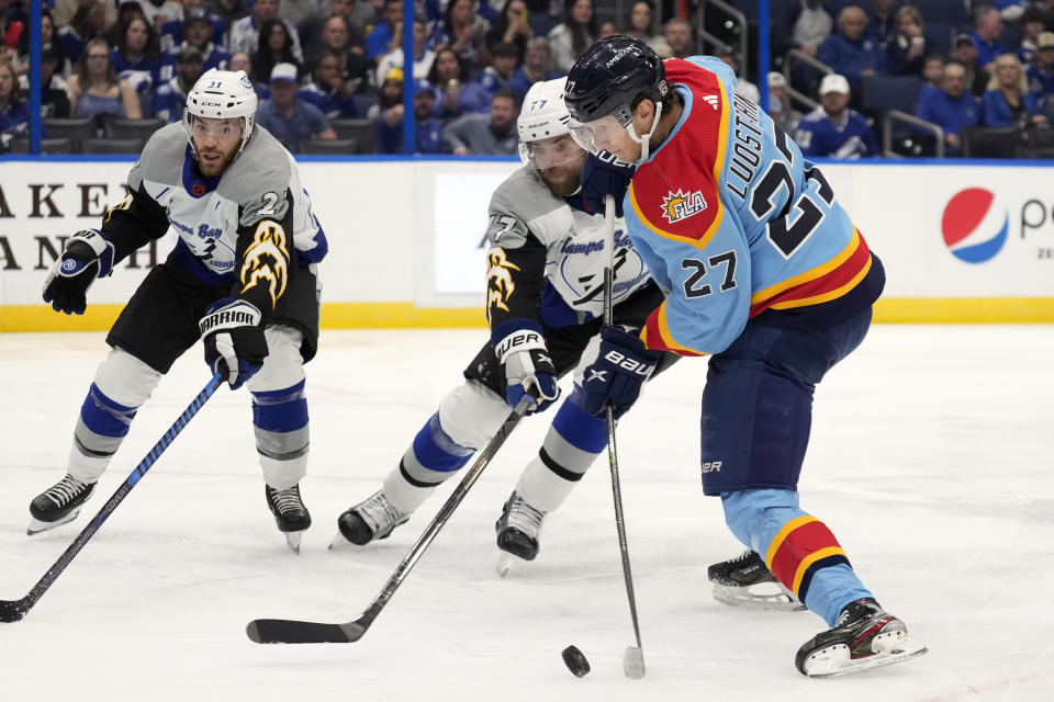 Florida Panthers center Eetu Luostarinen (27) gets off a shot in front of Tampa Bay Lightning defenseman Victor Hedman (77) and center Brayden Point (21) during the first period of an NHL hockey game Saturday, Dec. 10, 2022, in Tampa, Fla. (AP Photo/Chris O'Meara)