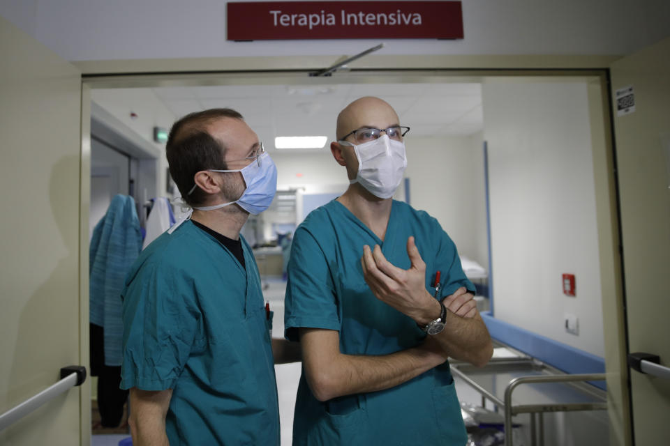 In this March 16, 2020, photo, Sergio Cattaneo, left, head of anesthesiology and intensive care of the Brescia Spedali Civili hospital, and ICU doctor Matteo Filippini talk with The Associated Press, in Brescia, Italy. Three weeks into Italy’s coronavirus crisis, Cattaneo has seen an unused ward outfitted into an intensive care unit in six days, a hospital laundry room converted into a giant stretcher-filled waiting room and a tented field hospital erected outside to test possible new virus patients. (AP Photo/Luca Bruno)