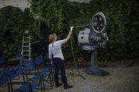 In this Monday May 25, 2020 photo Christina Tsouta cleans an old projector on display at the Zephyros open-air cinema that specializes in films from past decades in Athens' central Petralona district. Like so much else, Greece's open-air cinemas, where patrons can enjoy a movie in the flower-scented moonlight with a drink, a snack and even a smoke, have been hard-hit by lockdown measures. Under the country's partial reopening, open-air cinemas started operating on June 1, a month late and with considerable restrictions. (AP Photo/Petros Giannakouris)